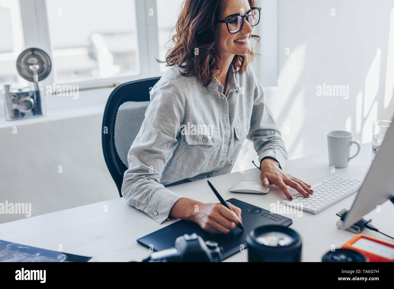 Joven fotógrafo que trabaja en equipo con Bloc de dibujo en el escritorio de oficina. Joven mujer caucásica con tableta gráfica digital y dibujo a lápiz Foto de stock
