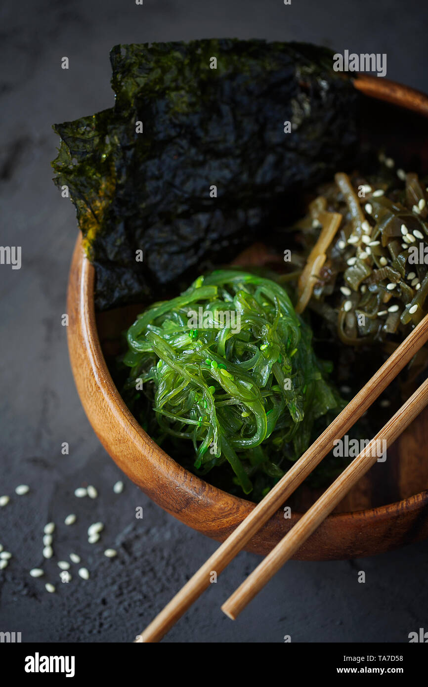 Aperitivo japonés tradicional - Chuka Wakame algas nori tostada crujiente y ensalada de hojas en el tazón de madera sobre fondo oscuro de cerca vista superior Foto de stock