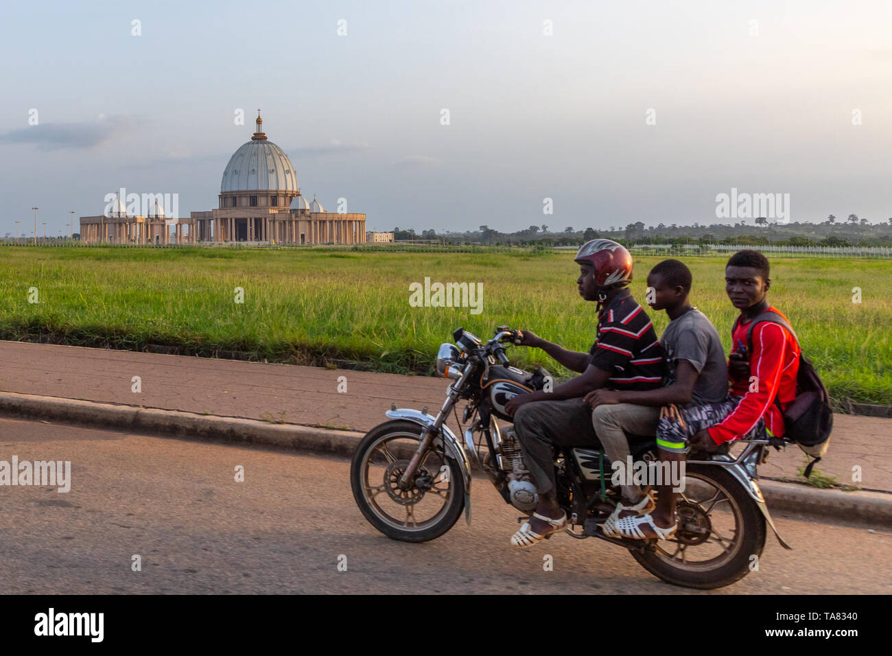 los-hombres-africanos-en-una-moto-pasando-delante-de-la-basilica-de-nuestra-senora-de-la-paz-catedral-cristiana-region-des-lacs-yamoussoukro-costa-de-marfil-ta8340.jpg