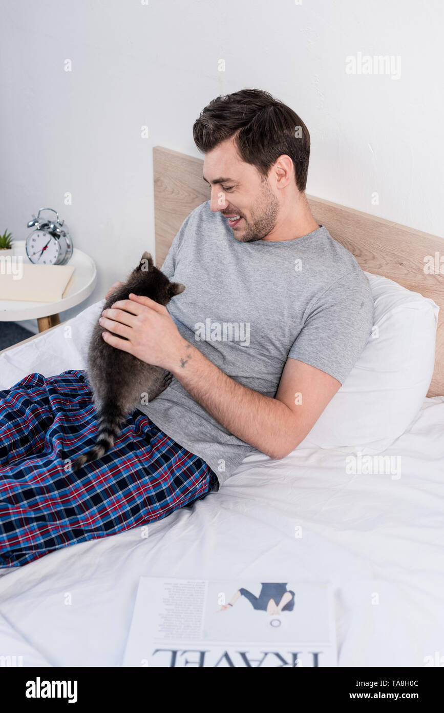 Guapo en Pijama sonriente relajado la cama con gracioso mapache Fotografía de - Alamy
