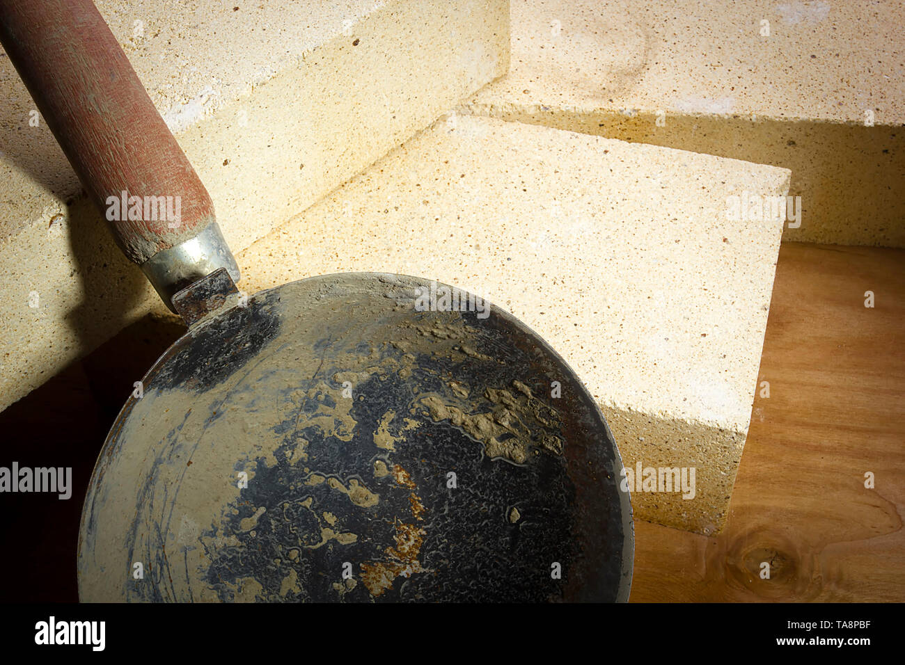 Cuchara de mortero y ladrillos refractarios sobre una superficie de madera Foto de stock