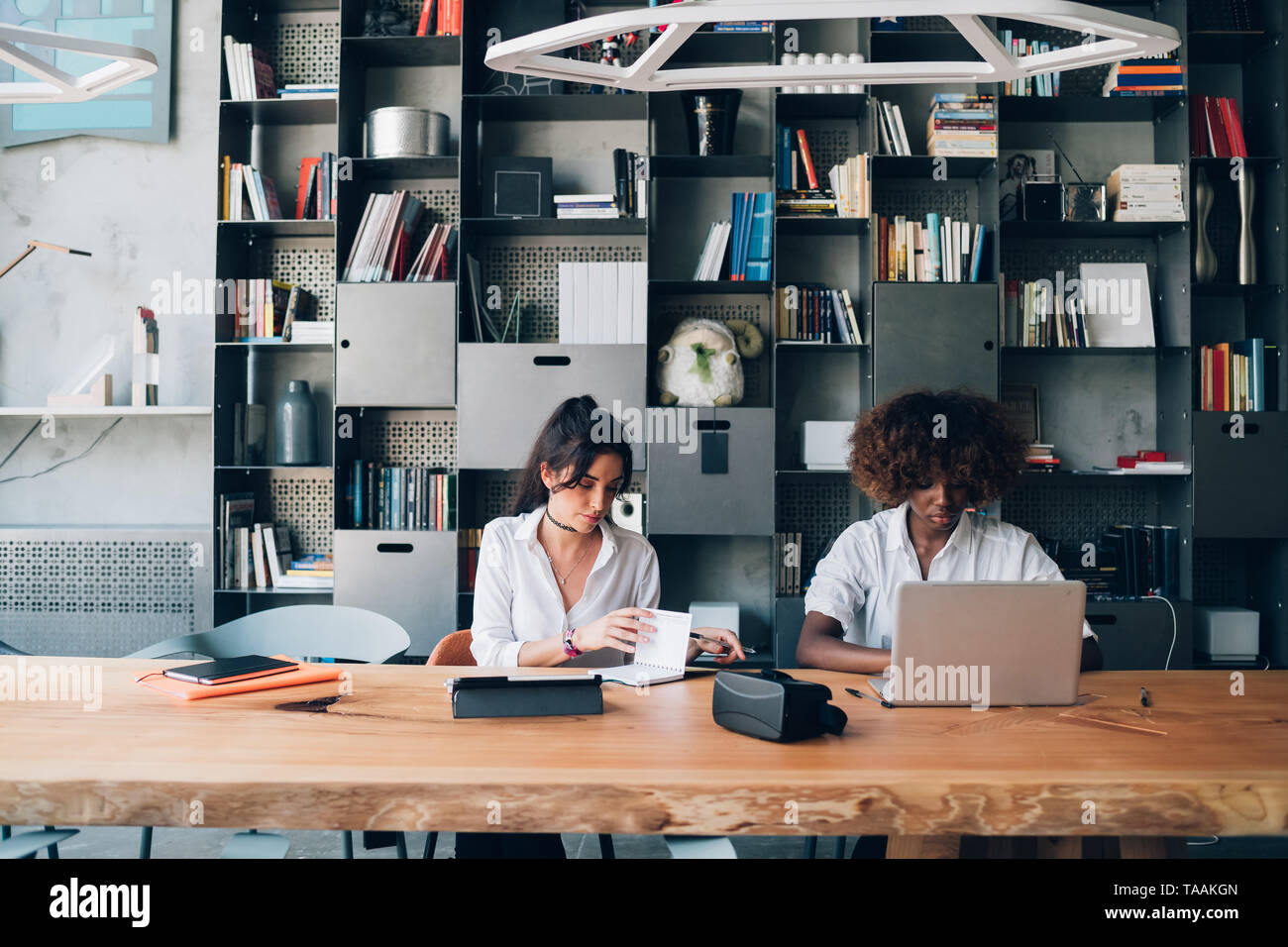 Dos mujeres jóvenes estudian juntos en la moderna oficina coworking- ingeniosos, innovación, tecnología Foto de stock