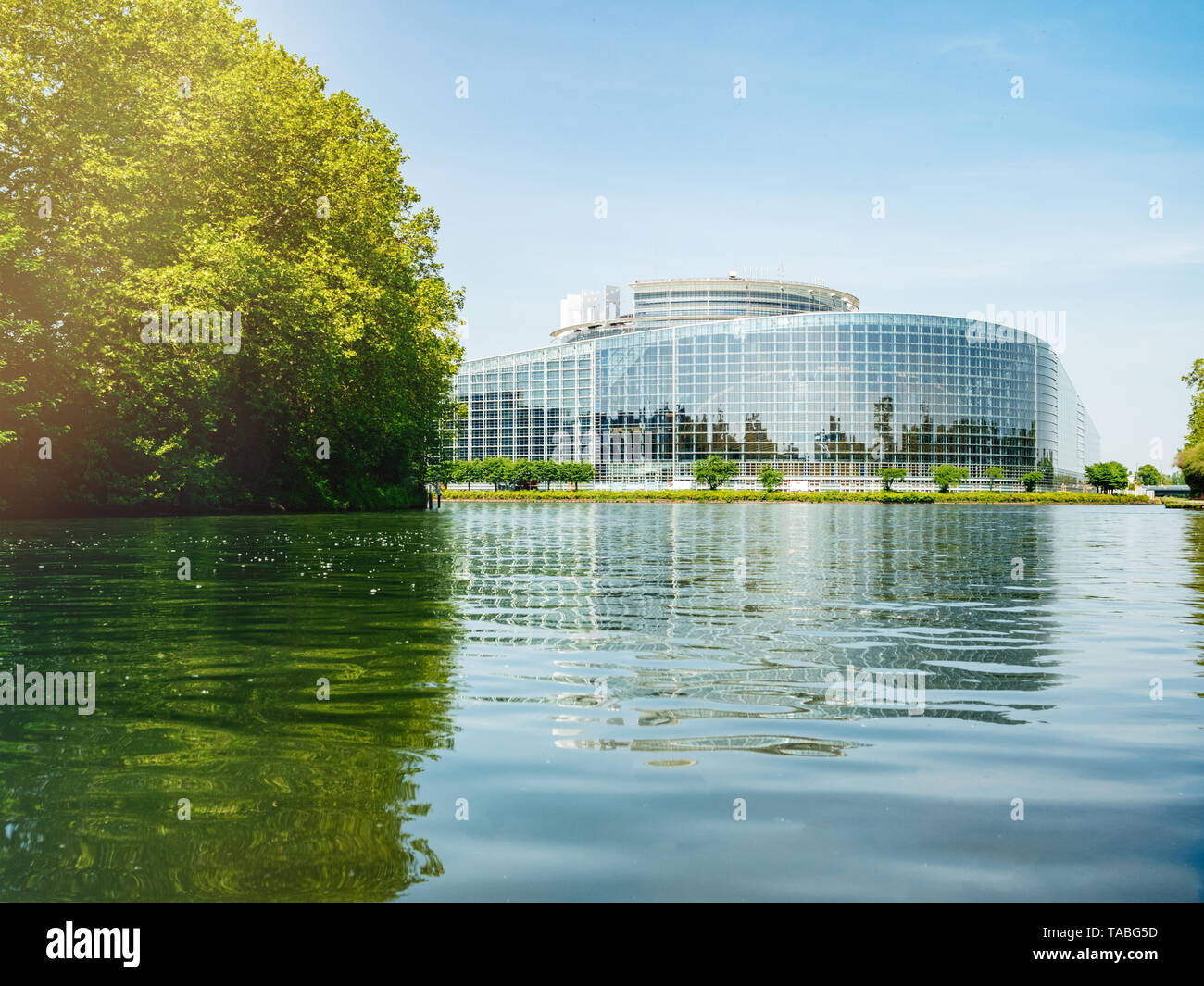 Ángulo de visión baja de amplia fachada de la sede del Parlamento Europeo en Estrasburgo, un día antes de la elección al Parlamento Europeo de 2019 - clear blue sky y la calma del agua del río Ill llamarada solar. Foto de stock