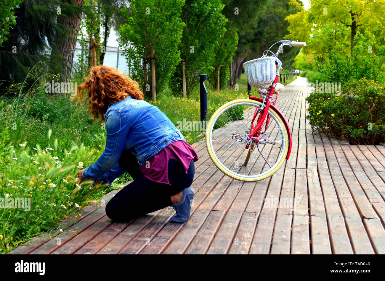 Mujer rubia caminando en el parque con un azul denim en una bicicleta roja Foto de stock