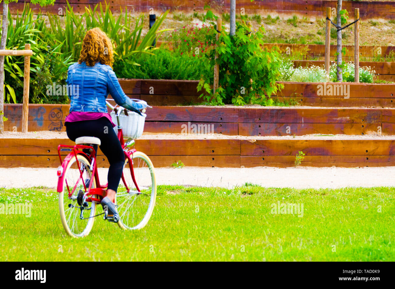 Mujer rubia caminando en el parque con un azul denim en una bicicleta roja Foto de stock
