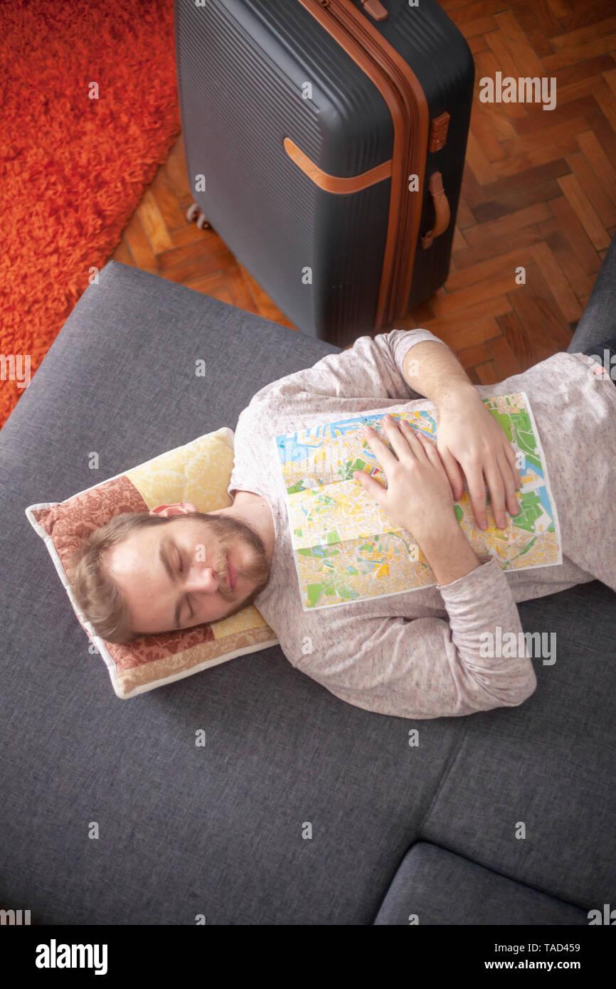 Un joven viajero - dormir con un mapa de la ciudad en su pecho, mientras  descansa en el interior sobre una cama. Maleta cerca Fotografía de stock -  Alamy