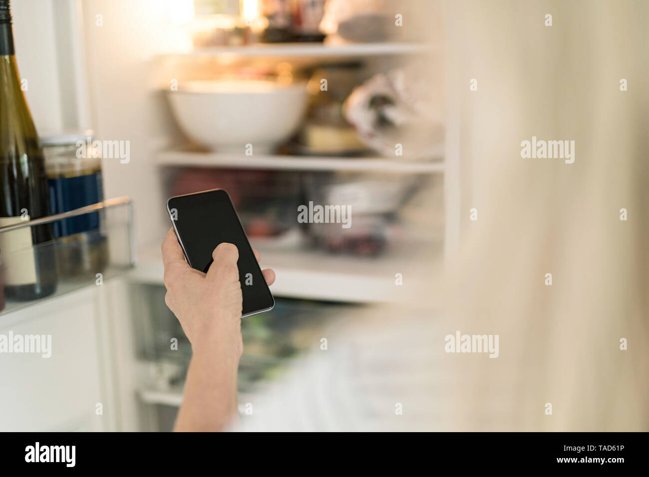 Mano de mujer con smartphone comprobando la nevera en la cocina en el hogar inteligente Foto de stock