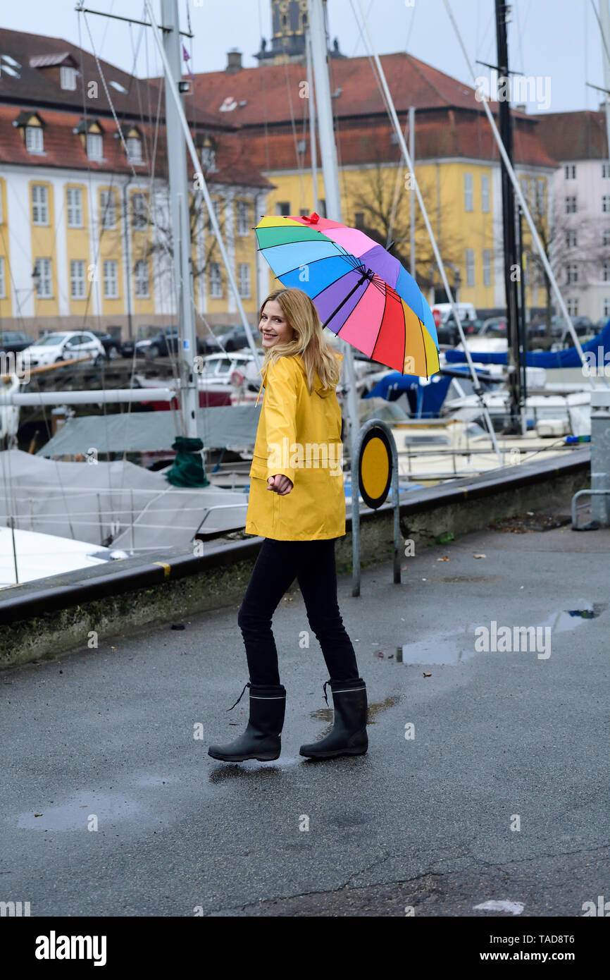 Dinamarca, Copenhague, mujer alegre y con coloridos paraguas paseando en el puerto de la ciudad Foto de stock