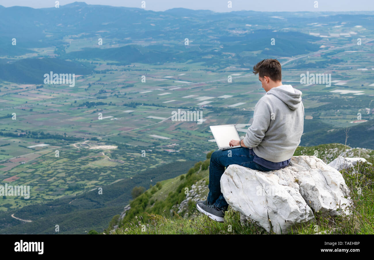Hombre Joven Sentado En La Cima De La Montana Con Vistas A Los Campos Y Colinas Y Trabajando En Linea Concepto De Cobertura De Banda Ancha De La Red Celular 5g Fotografia