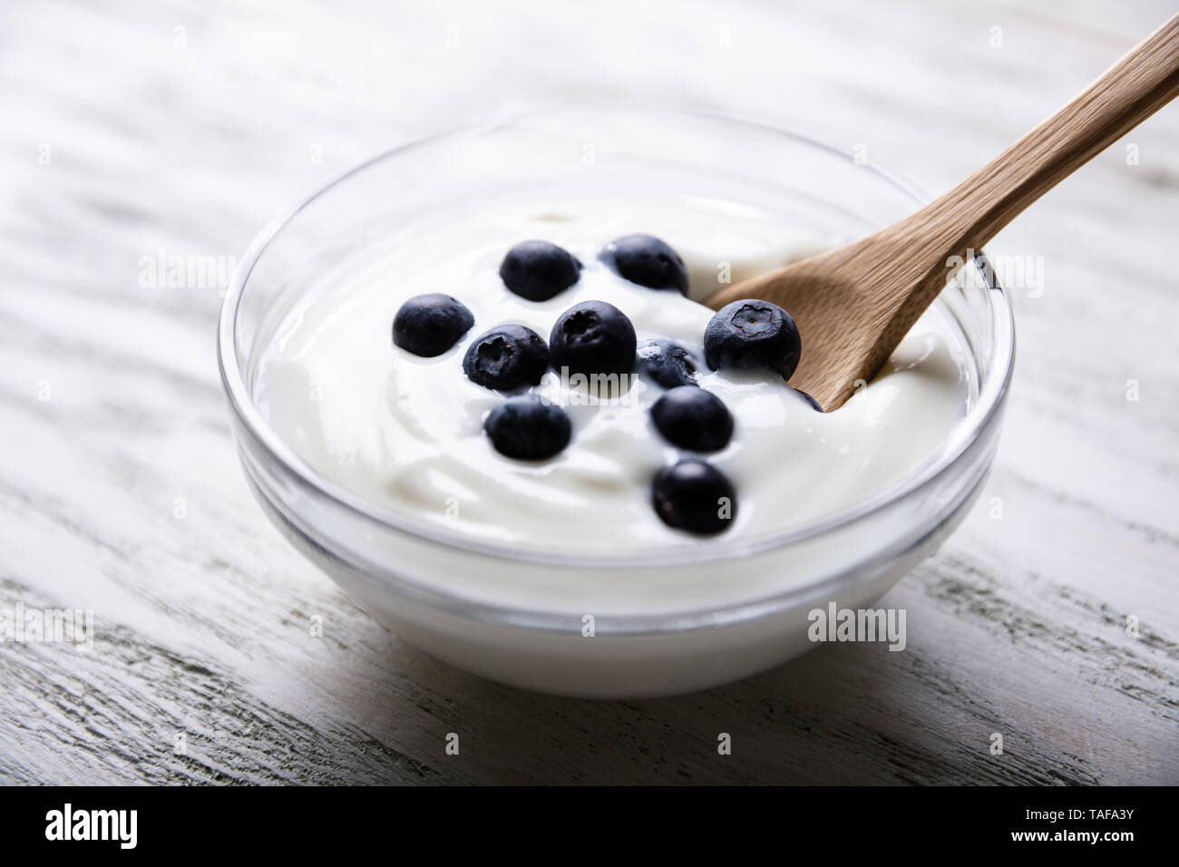 Blanco en un tazón de yogur con arándanos cerca de cuchara de madera sobre la mesa Foto de stock
