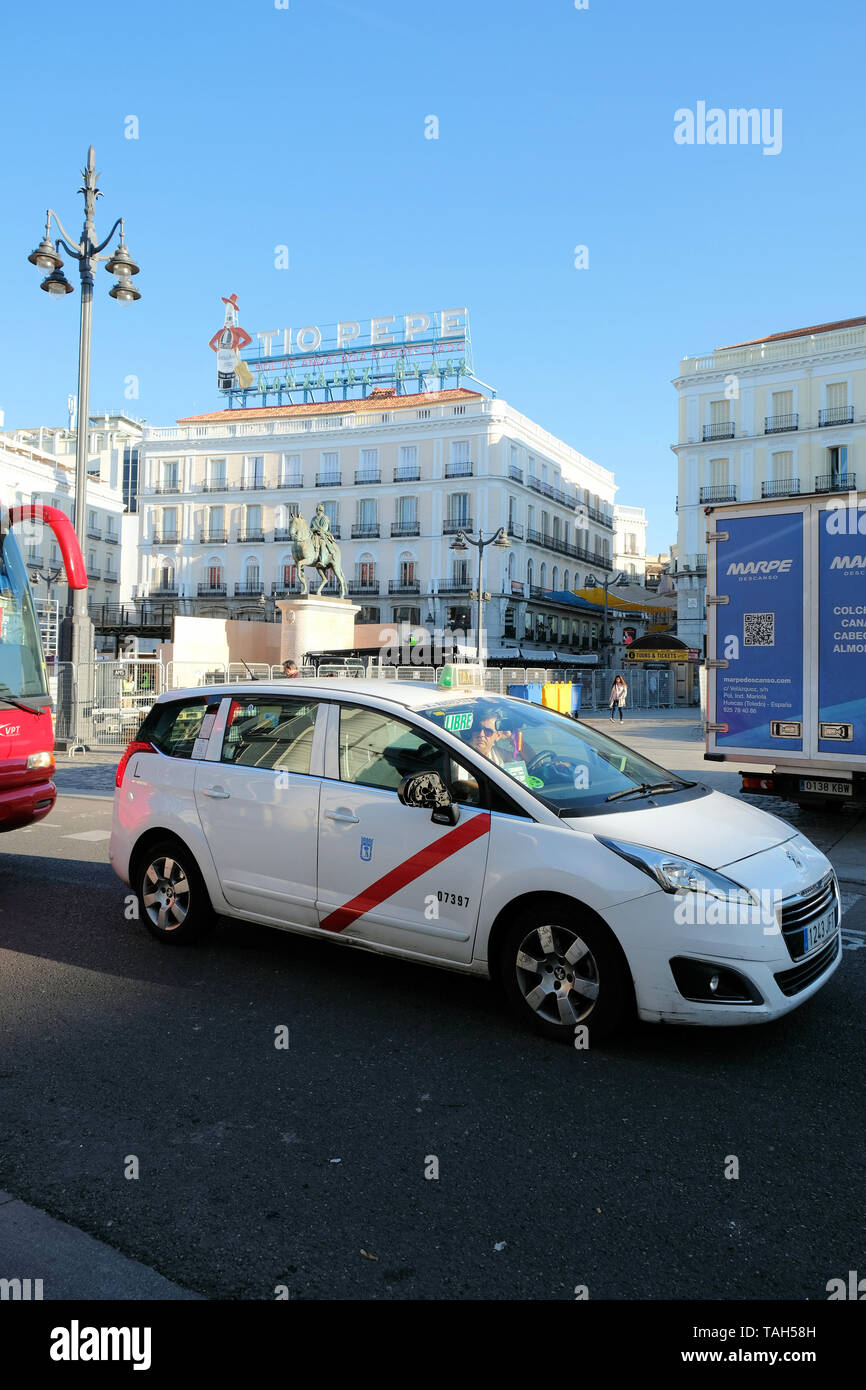 Patológico Redondo Almuerzo Taxi esperando en el tráfico delante de la plaza de la Puerta del Sol en  Madrid, España; icónico Tio Pepe signo de neón y la estatua de Carlos III  en el fondo