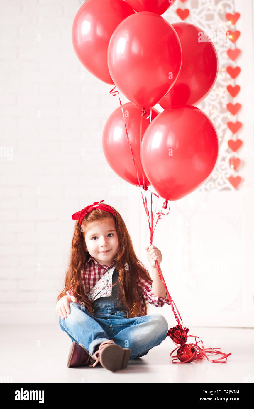 Lindo bebé niña 3-4 años de la celebración de los globos rojos sentados en  el piso n white room. Mirando a la cámara. Fiesta de cumpleaños Fotografía  de stock - Alamy