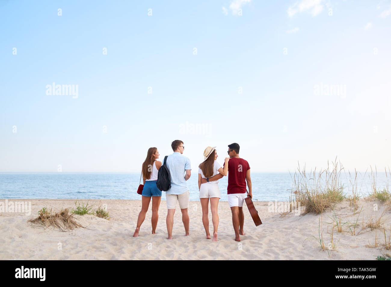Un grupo de amigos, ir a la playa al atardecer. Los jóvenes hombres y  mujeres que caminan a la orilla para relajarse cerca del mar y tocar la  guitarra. Los adolescentes de