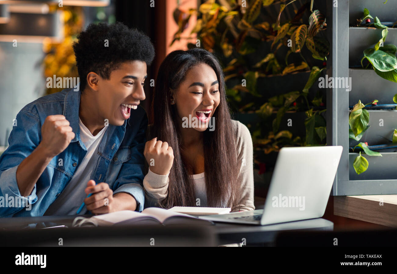Dos estudiantes eufóricos negro viendo los resultados de los exámenes en portátil Foto de stock