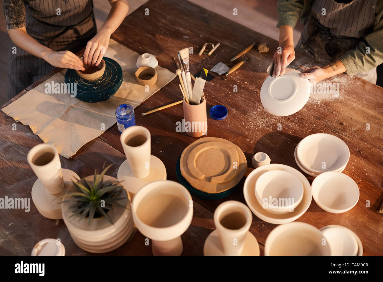 Close-up de irreconocible mujeres artesanas en delantales sentado en la mesa de madera, y trabajar con la cerámica en el taller Foto de stock