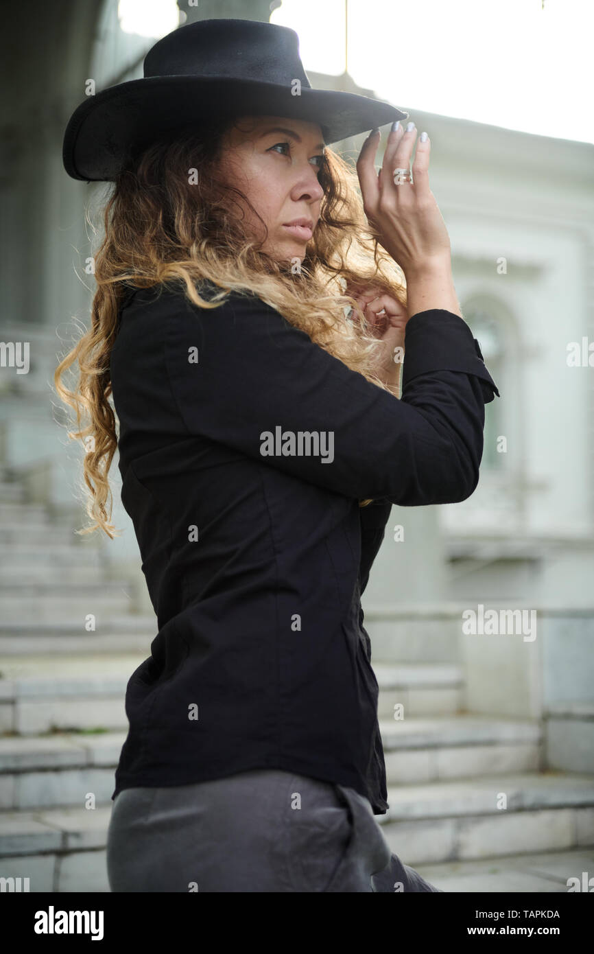 Chica de moda vestido con camisa negra, sombrero y pantalón ancho posando  cerca de la vieja casa blanca Fotografía de stock - Alamy