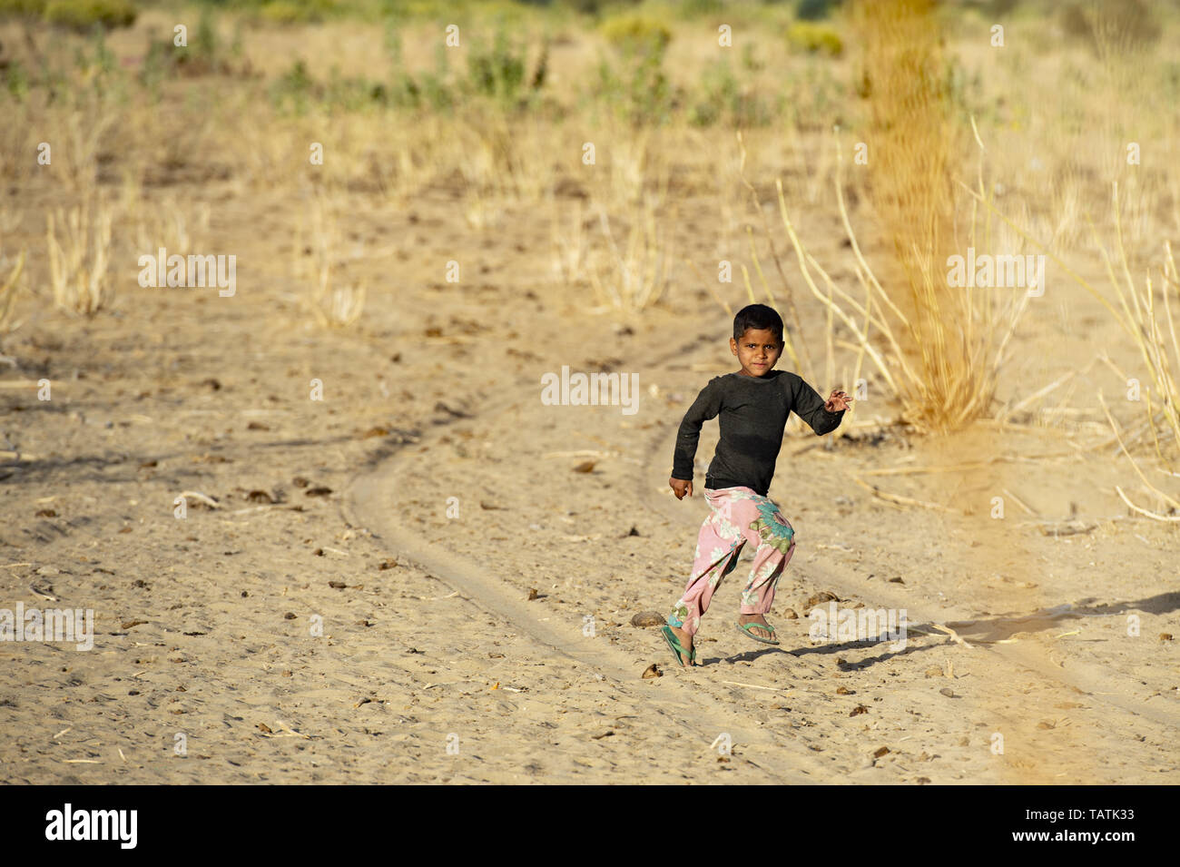 Un lindo niño corre a su aldea en el medio del desierto de Thar. Foto de stock