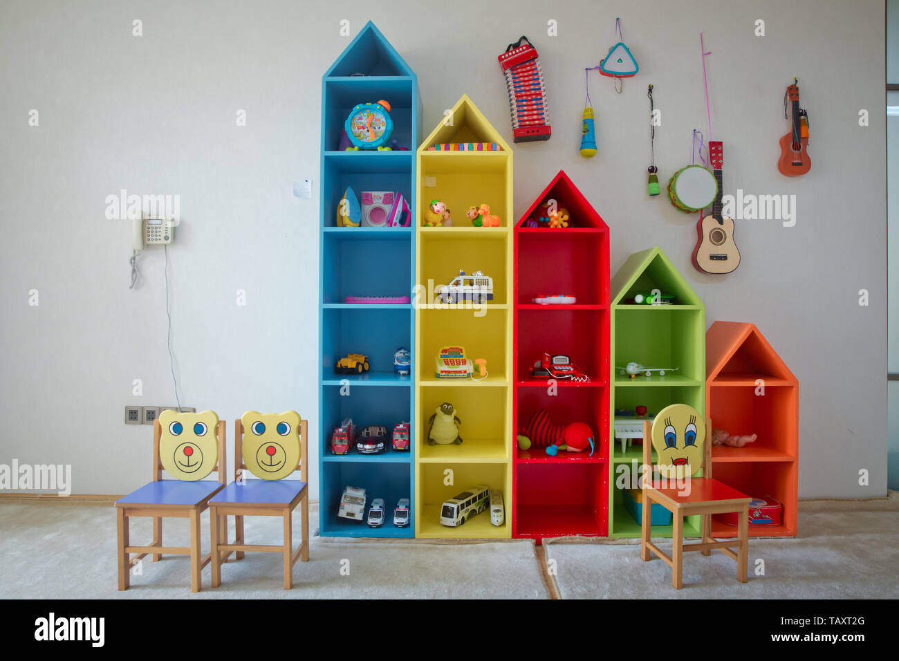 La bebé con estantes con juguetes . Los niños photosession antecedentes. Sala de juegos para niños con coloridos educativos juguetes plástico.Juegos Piso para p Fotografía de stock -