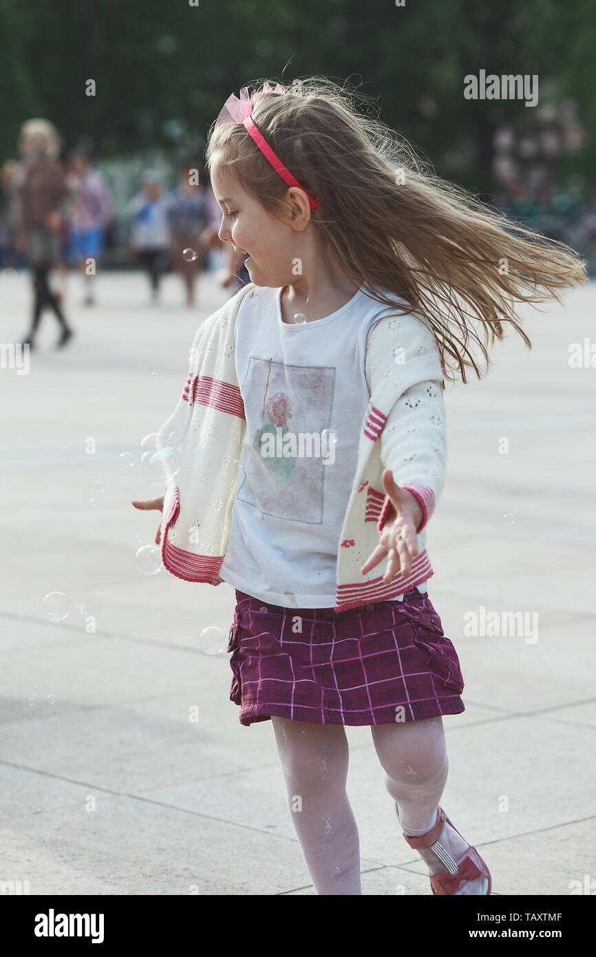 Poco feliz, la niña jugando con las pompas de jabón en el centro de la  ciudad. Niños corriendo alrededor y atrapar las burbujas de jabón. Personas  sinceras, momentos reales Fotografía de stock 