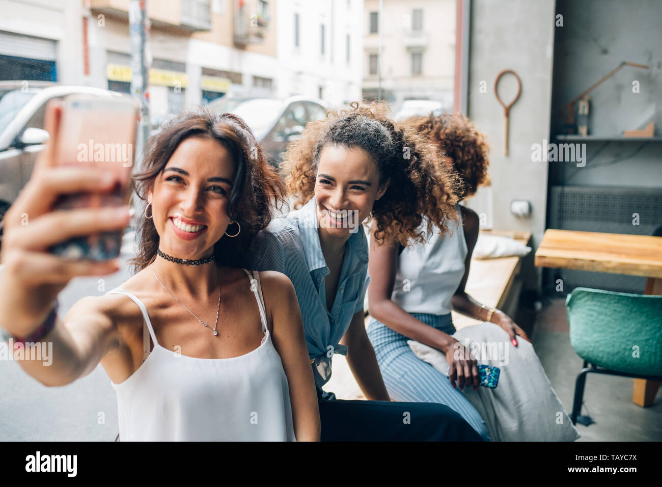 Tres jóvenes mujeres tomando la foto con el smartphone y divirtiéndose en coworking oficina - amusement, alegre, relación Foto de stock