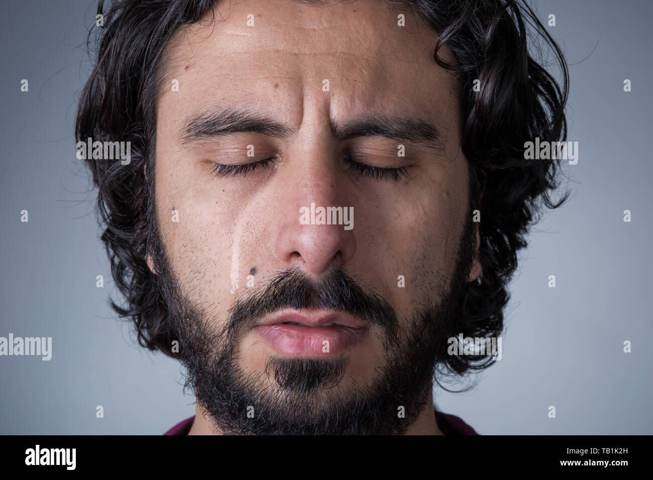 El hombre con la barba y el pelo largo llorando con los ojos cerrados Foto de stock