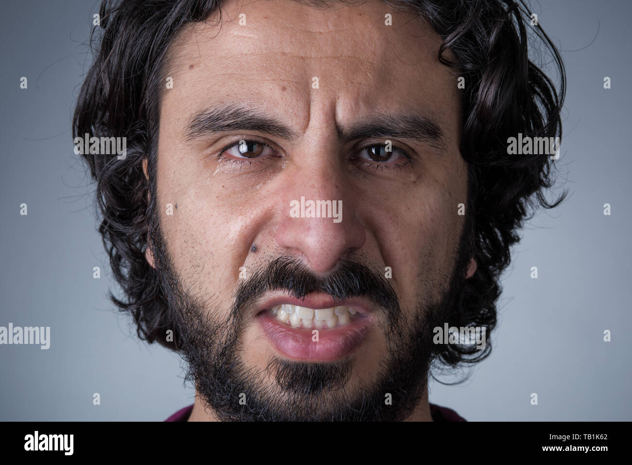 El hombre enojado con barba y cabello largo llanto mirando a la cámara Foto de stock