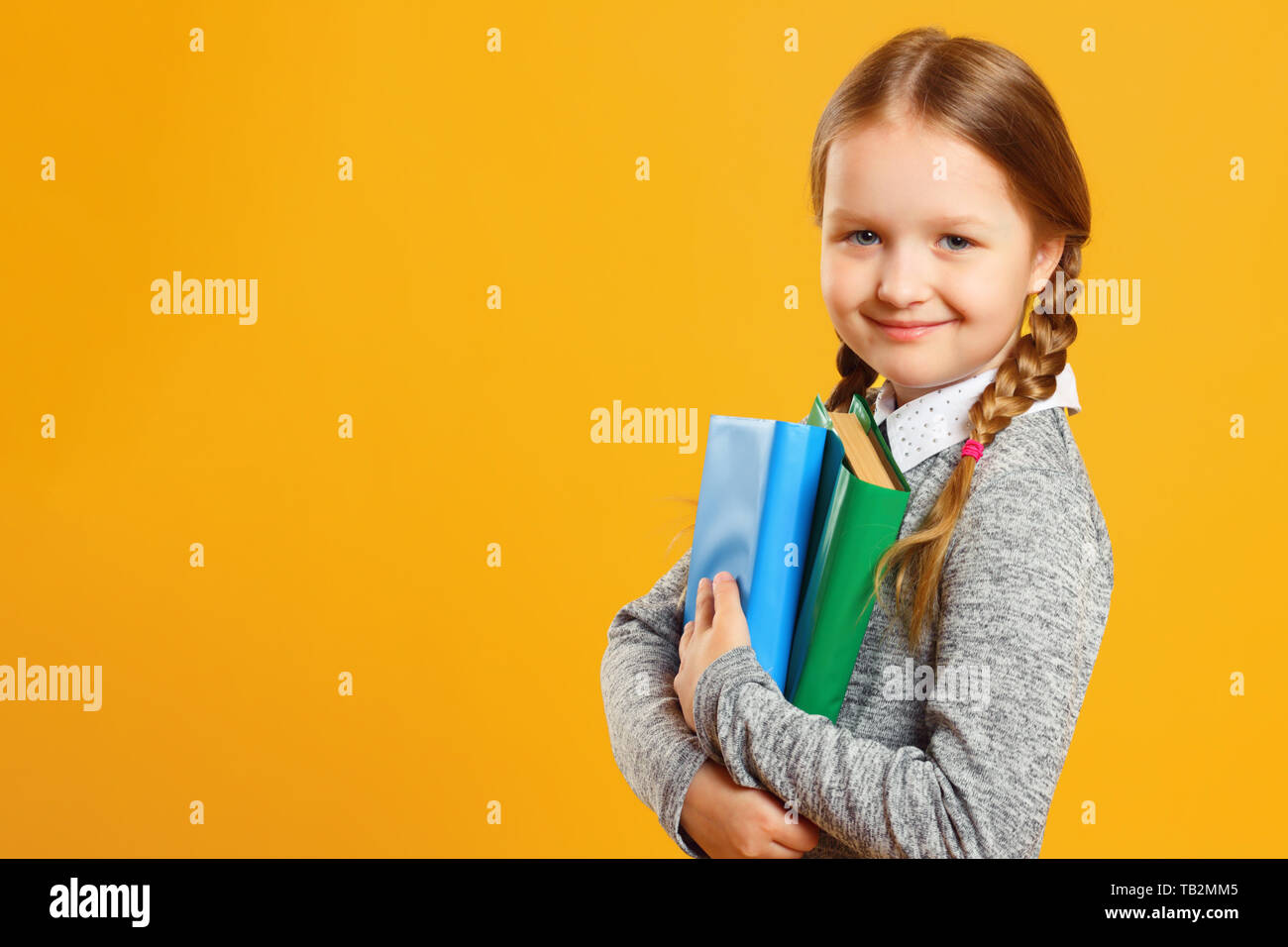 Retrato de una niña colegiala con pigtails sobre un fondo amarillo. El niño contiene libros de texto. El concepto de la educación y de la escuela. Copie el espacio. Foto de stock