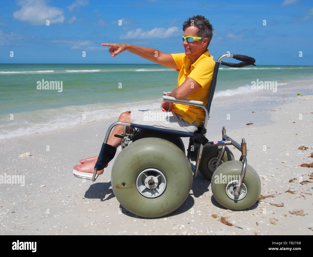 Mujer discapacitada en silla de ruedas de playa goza del sol y la arena en Honeymoon Island State Park, en Dunedin, Florida, EE.UU., 10 de mayo de 2019, © Katharine Andrioti Foto de stock