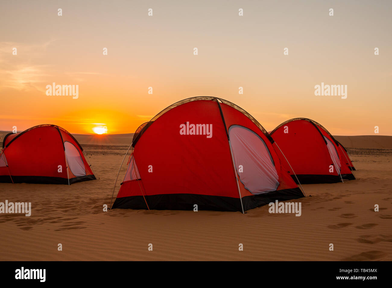 Tres Naranjas hombre dos carpas en el remoto desierto occidental de Sudán lanzó para la noche en la puesta de sol de color amarillo brillante con el sol en el horizonte Foto de stock