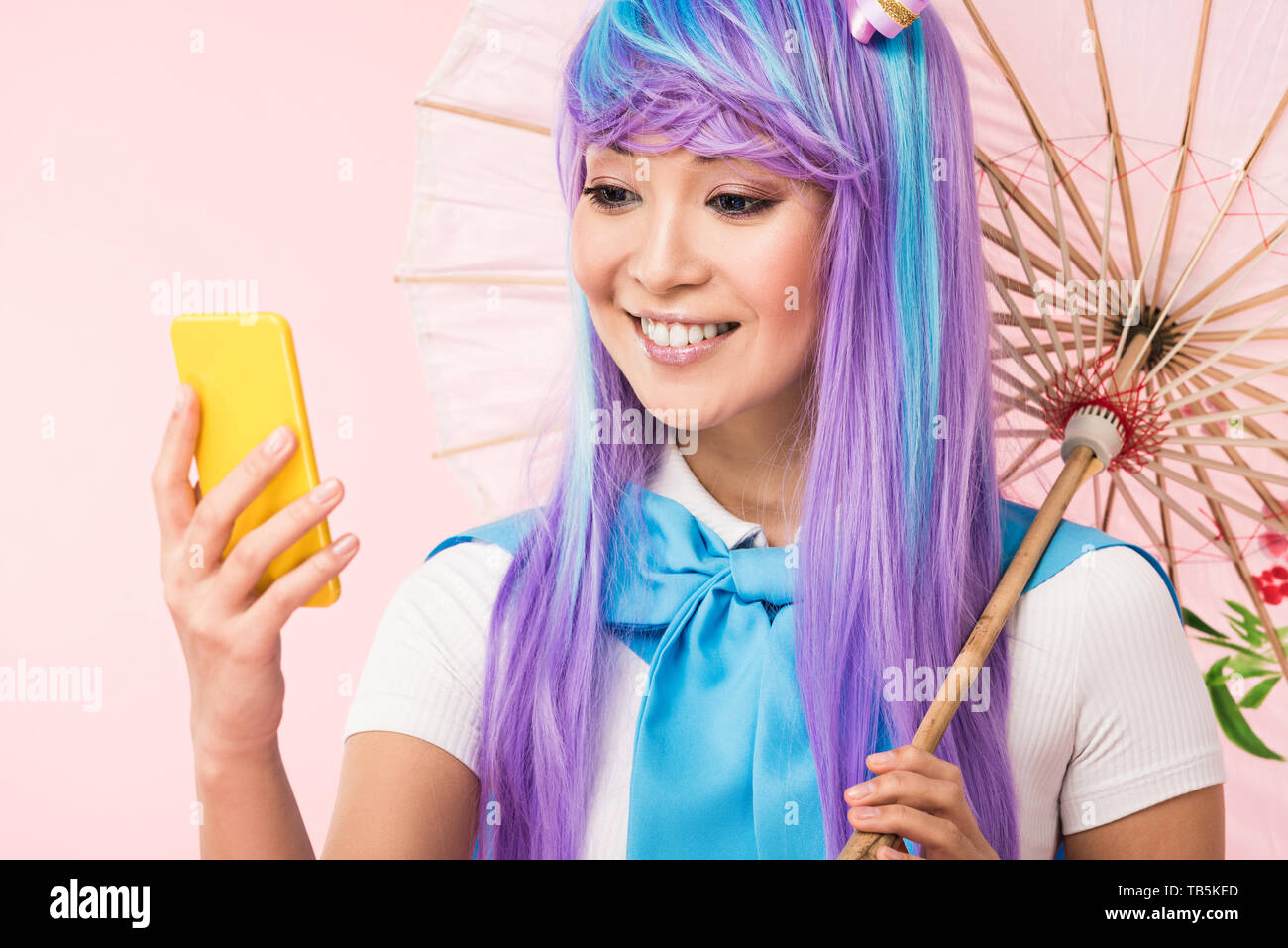 Anime asiático sonriente chica con paraguas de papel mirando smartphone  aislado en rosa Fotografía de stock - Alamy