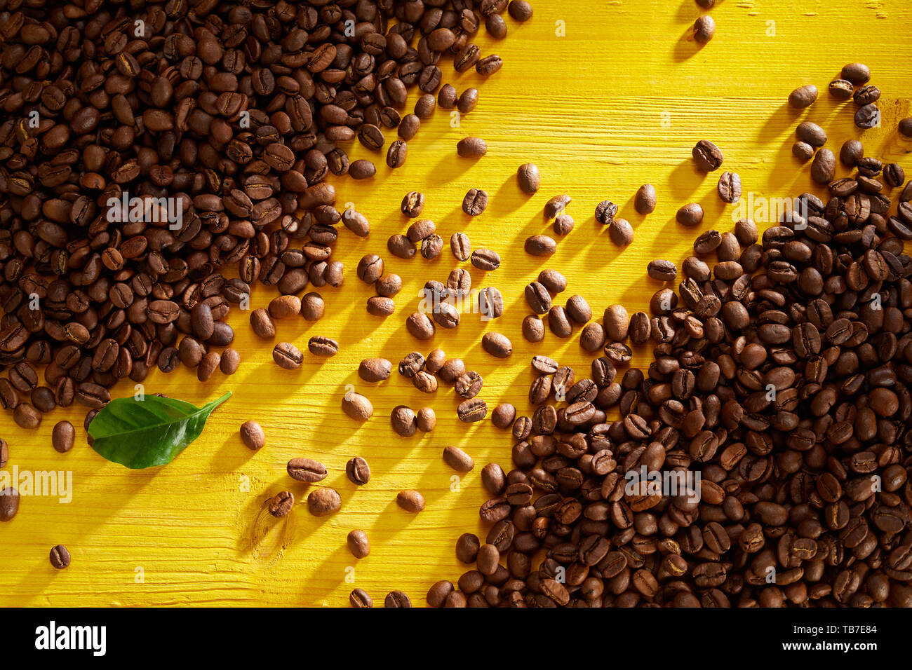 Los granos de café tostado fresco en esquinas opuestas con línea diagonal entre sobre un fondo de madera amarilla en una vista aérea Foto de stock