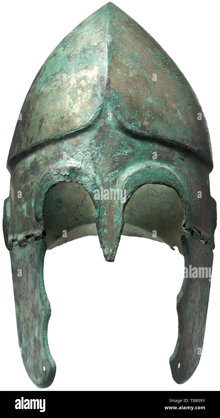 Un casco Chalcidian, tipo V, a comienzos del siglo IV a.C., casco de bronce con predominantemente preservada, full-face chapado de estaño. El borde decorado en el ojo y el oído escotaduras con una costilla contorneada sobresalientes. Una lanceta protector nasal en forma de establecer entre los ojos. Ligeramente arqueado cuello guard desplazamiento desde el cráneo por una pequeña curva. El cráneo con una cresta medial dividiendo la parte superior en dos planteadas, lóbulos semiesférica. El borde carinated peaking contorneada en una "V" invertida por encima de la ranura de la ceja. La mejilla trozos con dos escotaduras conectado al mundo antiguo, Additional-Rights-Clearance-Info-Not-Available Foto de stock