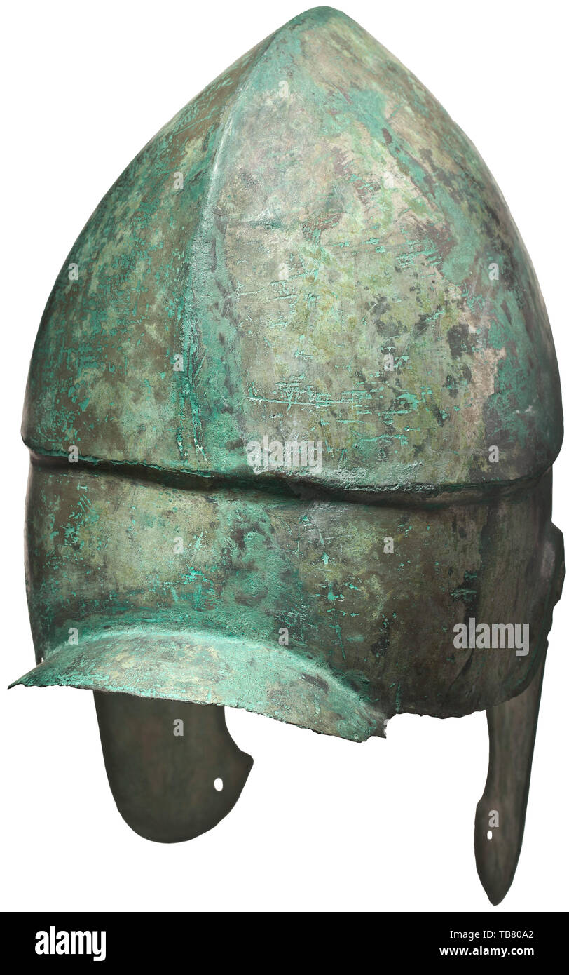 Un casco Chalcidian, tipo V, a comienzos del siglo IV a.C., casco de bronce con predominantemente preservada, full-face chapado de estaño. El borde decorado en el ojo y el oído escotaduras con una costilla contorneada sobresalientes. Una lanceta protector nasal en forma de establecer entre los ojos. Ligeramente arqueado cuello guard desplazamiento desde el cráneo por una pequeña curva. El cráneo con una cresta medial dividiendo la parte superior en dos planteadas, lóbulos semiesférica. El borde carinated peaking contorneada en una "V" invertida por encima de la ranura de la ceja. La mejilla trozos con dos escotaduras conectado al mundo antiguo, Additional-Rights-Clearance-Info-Not-Available Foto de stock