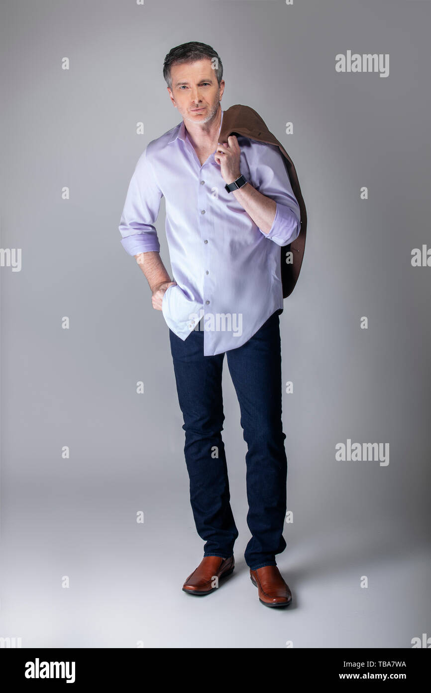 Empresario de mediana edad vistiendo ropa casual de negocios. El hombre está posando con untucked camisa manga larga con jeans sosteniendo chaqueta. Muestra Fotografía de stock - Alamy
