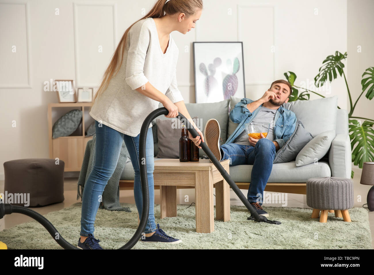 Esposa Limpieza piso mientras su marido perezoso viendo la televisión en casa Foto de stock