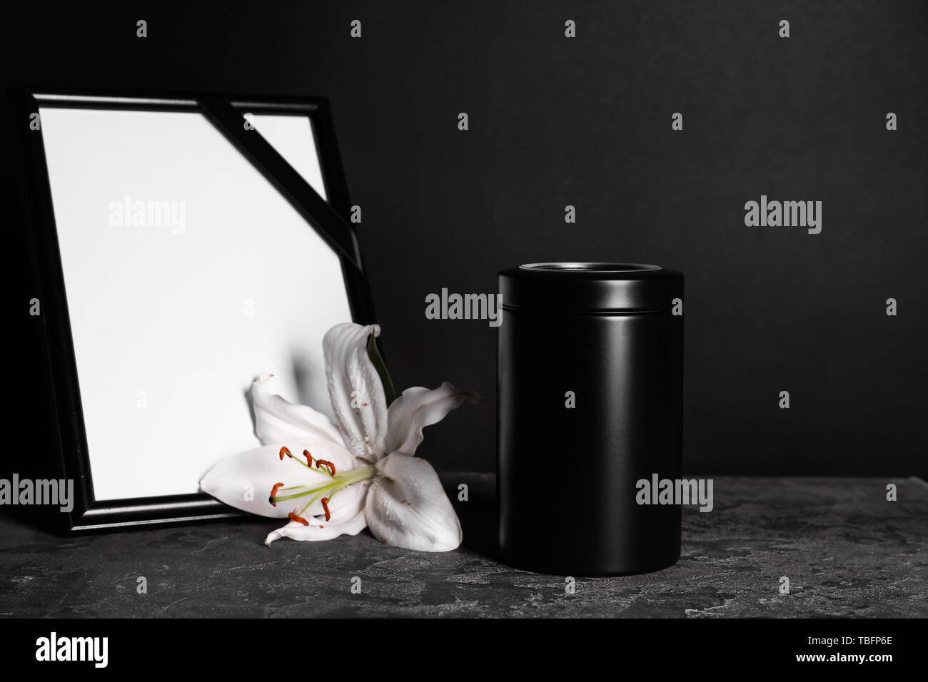 Urna funeraria con flor de lis y el bastidor en la tabla contra el fondo  oscuro Fotografía de stock - Alamy