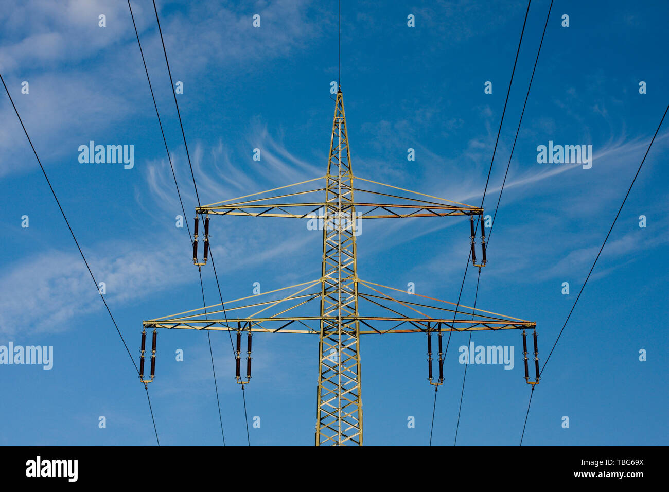 Parte superior de un poste eléctrico con el cielo azul y leves nubes cirrus. Foto de stock