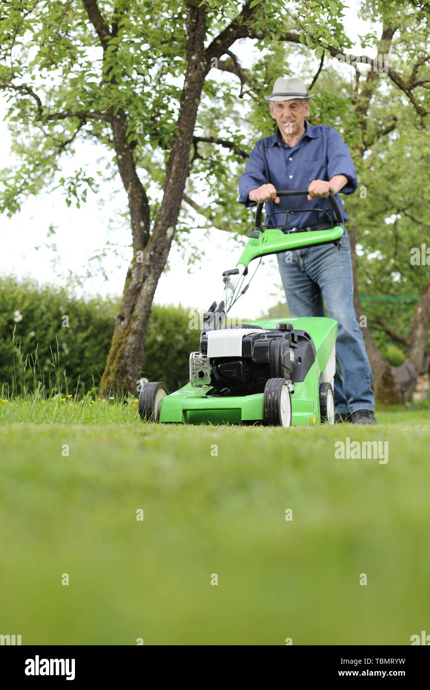 Un hombre trabajando con un cortacésped en su jardín Foto de stock