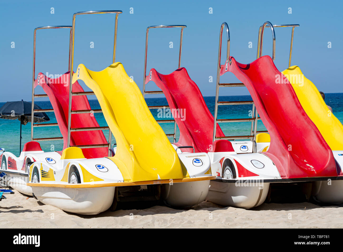 Coloridos botes de pedal con toboganes para alquilar en la playa de arena  con agua de mar azul Fotografía de stock - Alamy