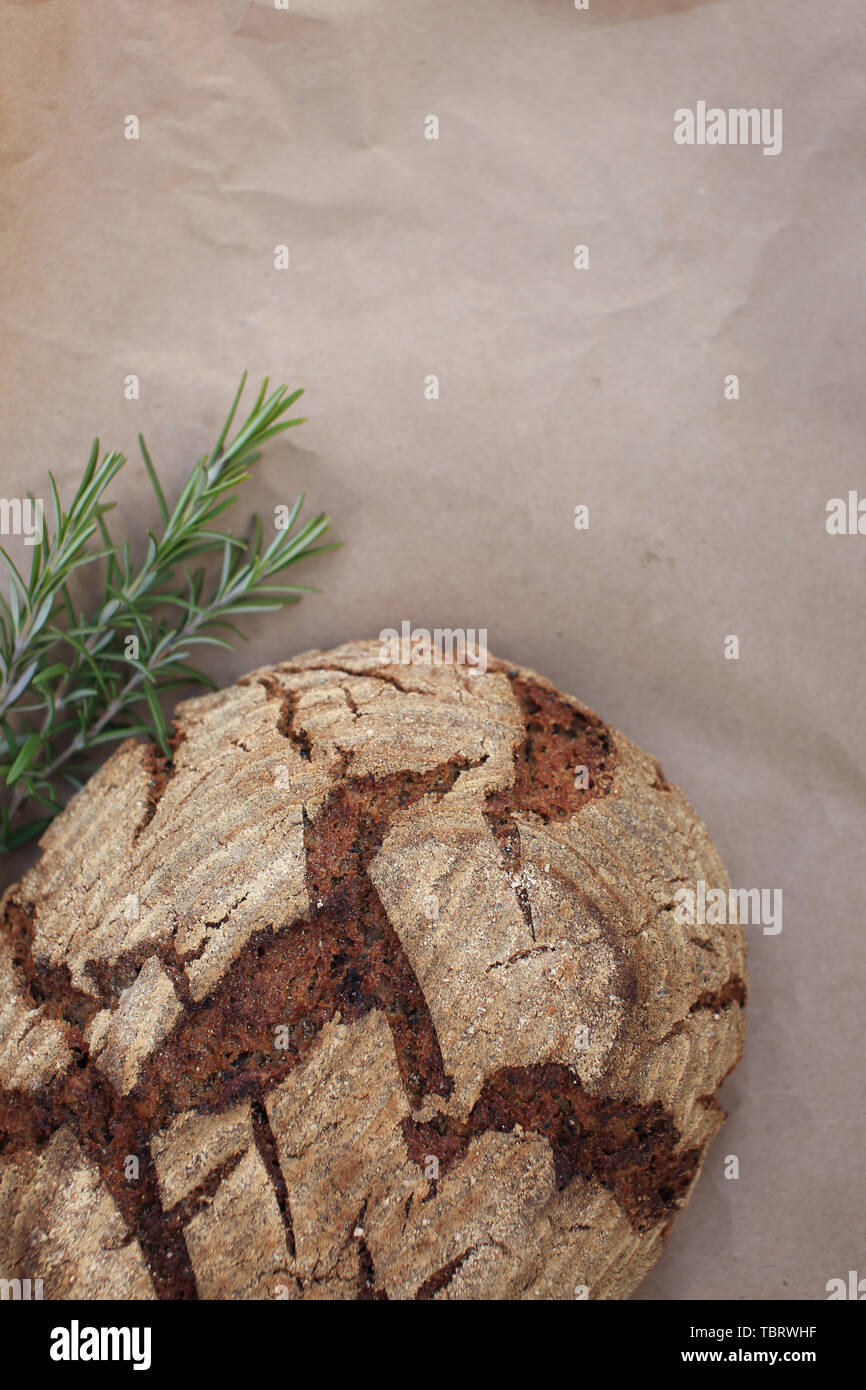 Bio grano entero pan casero hecho en masa agria puesta sobre papel kraft cerca de romero, rodada en estilo rústico. Foto de stock