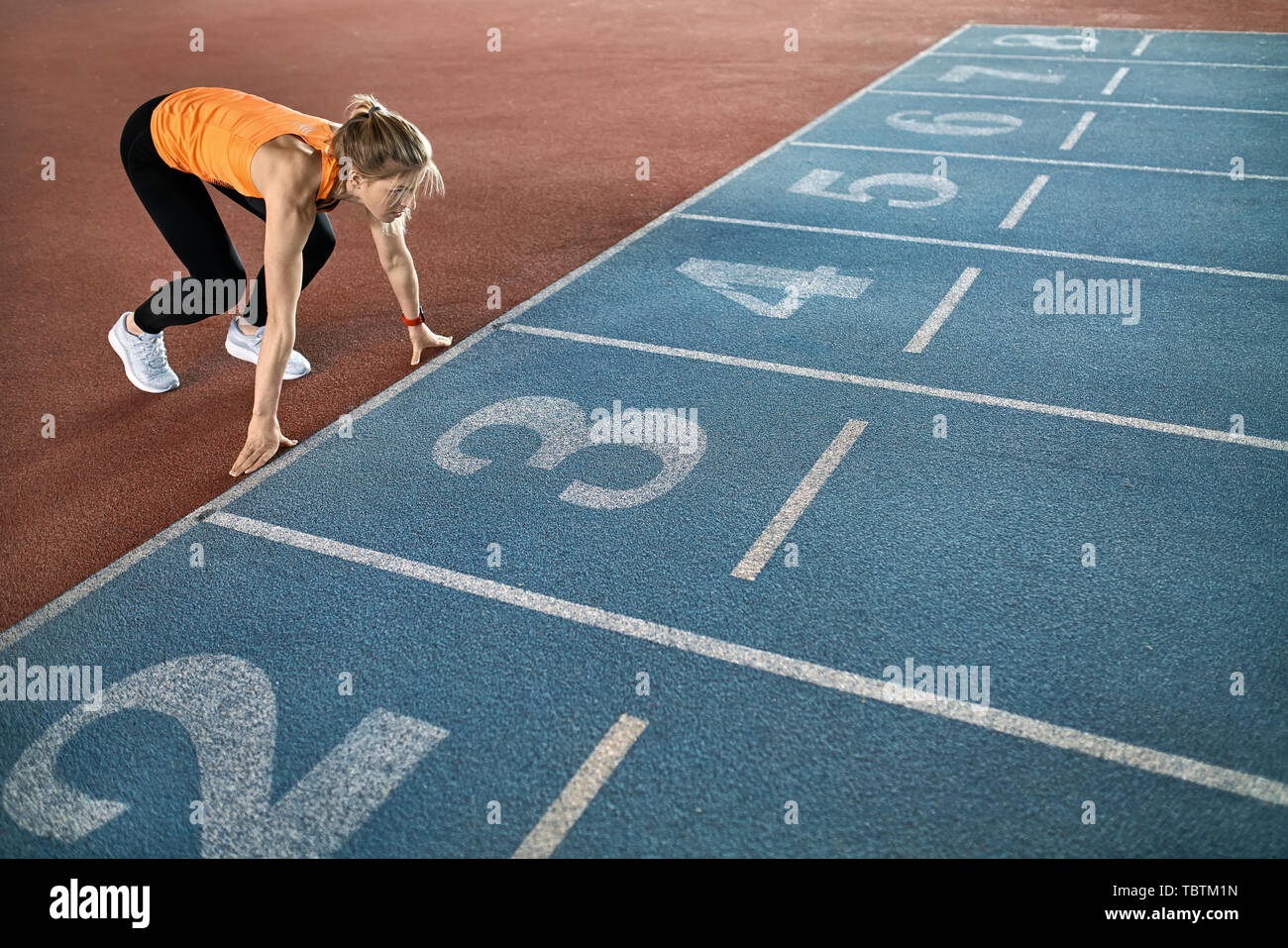Una niña asombrosa en una camiseta naranja con un pantalón negro y gris  está en la posición de inicio de tenis en la pista número 3 en el estadio.  Mira forw Fotografía
