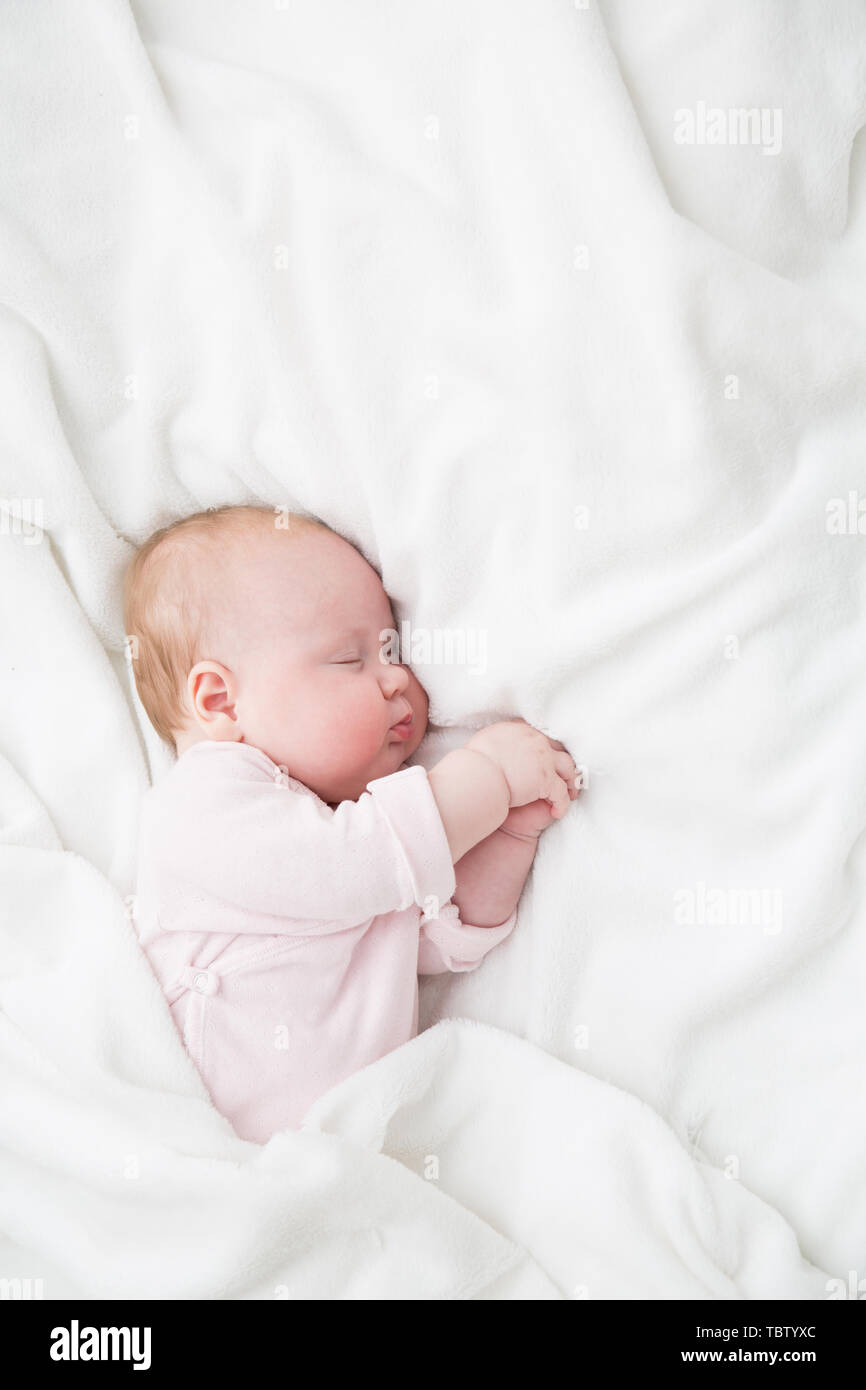 Bebe Durmiendo, 3 meses cabrito en tela rosa dormir sobre una sábana blanca, niño dormido en la cama Foto de stock