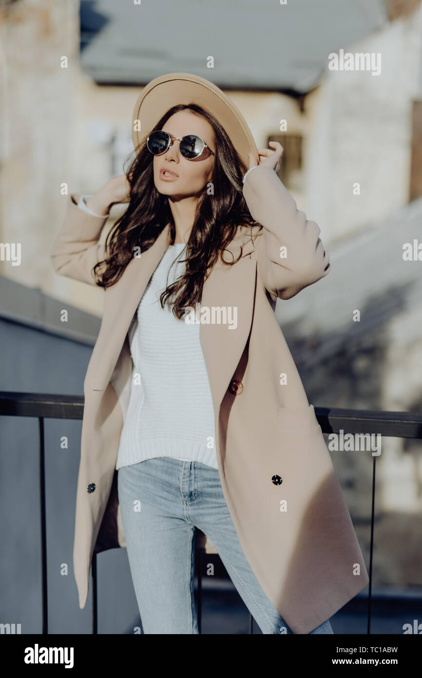 Retrato al aire libre de moda mujer hermosa joven posando en la calle.  Modelo vistiendo elegante capa gris, sombrero, gafas de sol redondo blanco.  Moda femenina c Fotografía de stock - Alamy
