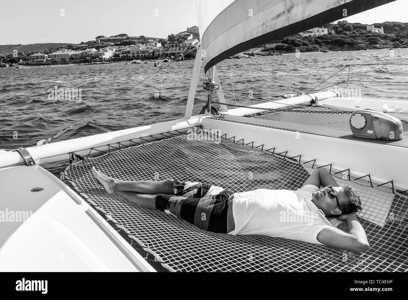 Hombre deportiva relajándose en un lujoso catamarán velero. Foto de stock
