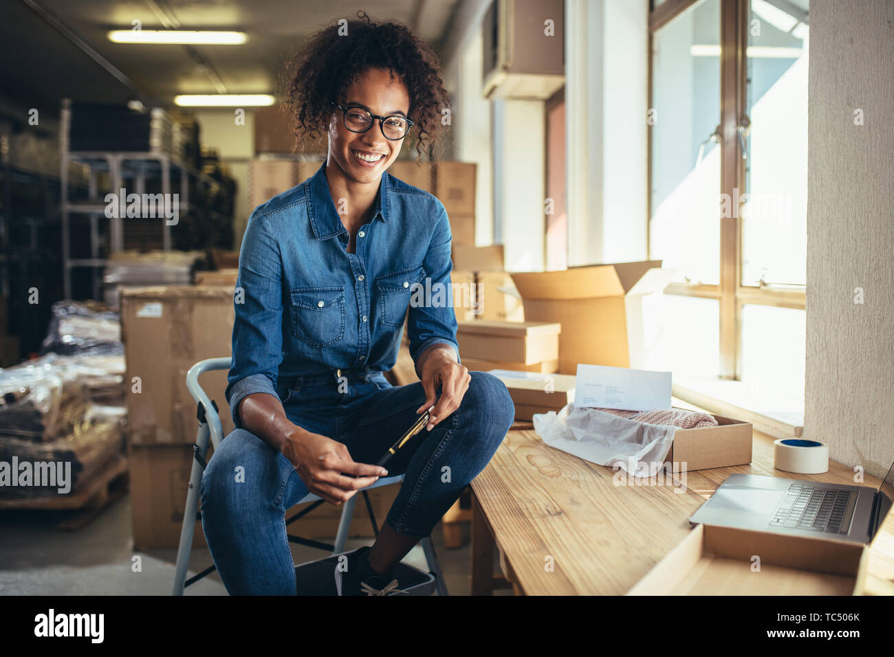 Mujer sonriente sentada en su lugar de trabajo. Seguro de propietario de negocio online mirando a la cámara y sonriendo. Foto de stock