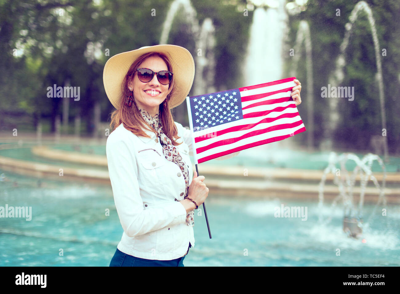 Feliz joven mujer patriota en hat estirando la bandera de Estados Unidos en el parque, el día de la independencia, el 4 de julio Foto de stock