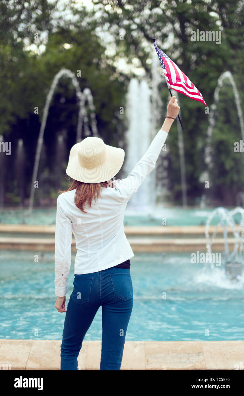 Mujer patriota en hat sosteniendo la bandera de EE.UU en park vista trasera, día de la independencia, el 4 de julio Foto de stock