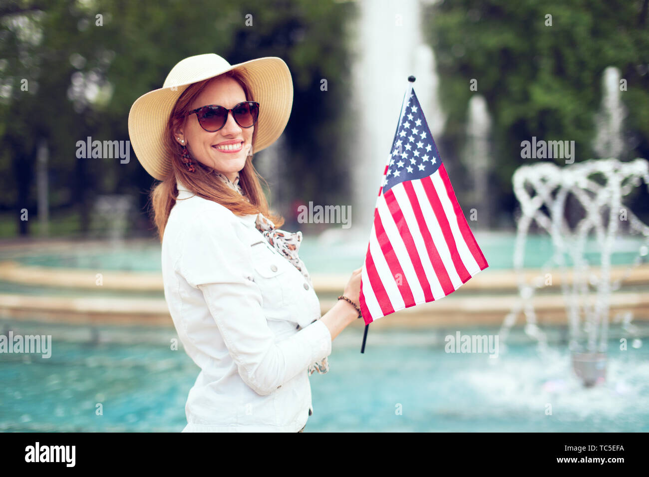 Joven mujer patriota en hat sosteniendo la bandera de EE.UU en estacionamiento en Fountain, día de la independencia, el 4 de julio Foto de stock