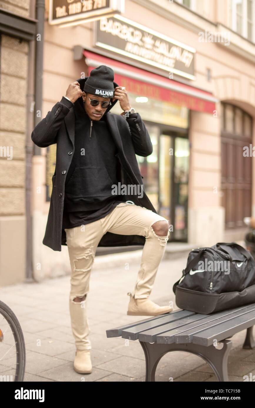 Hombre elegante en el banquillo en la calle, vistiendo ropa de estilo  urbano, visible, logotipos de marcas de ropa negra, Munich, Alemania  Fotografía de stock - Alamy