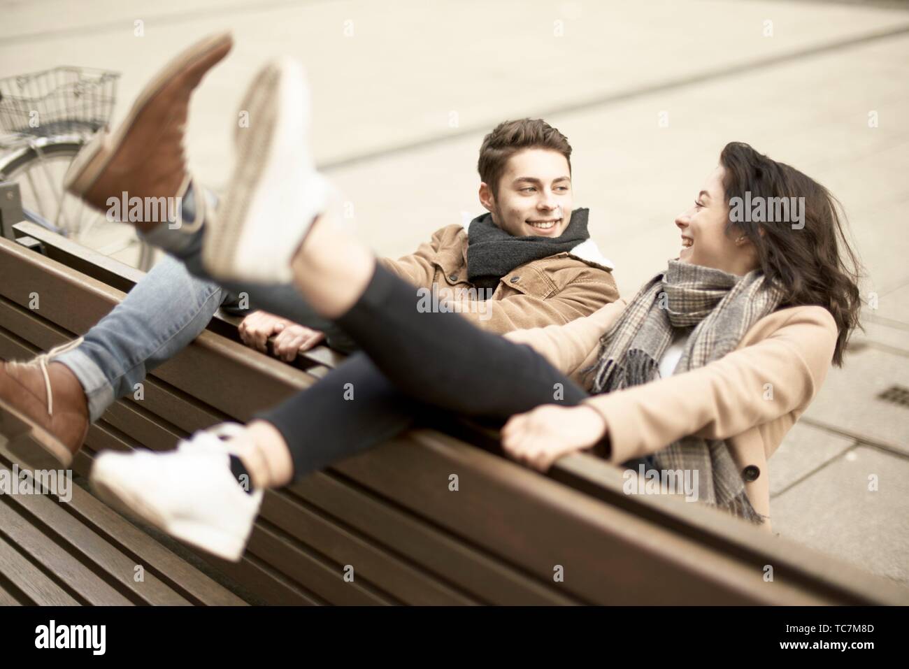 Sonriente joven pareja de adolescentes sentados en un banco al revés en ciudad, colgando juntos, patas arriba, boca abajo, en Cottbus, Brandenburgo, Foto de stock